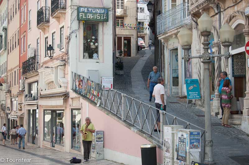 Two streets in coimbra filled with people walking, lines of buildings, and a man busking that you can see on a drive from Lisbon to Porto