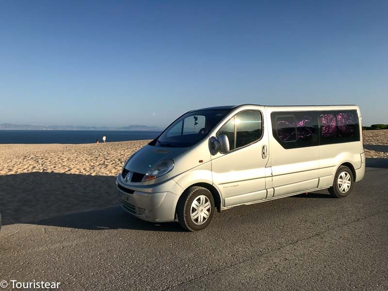 a rental white van on a paved road with a view of a sandy beach to save money on a road trip