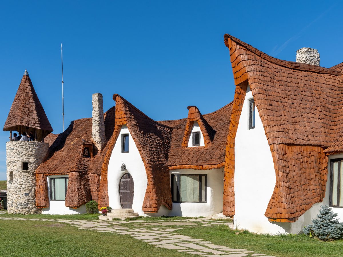 A white building with long tiled roof and a small tower of the Castelul de Lut Valea Zânelor in Transylvania