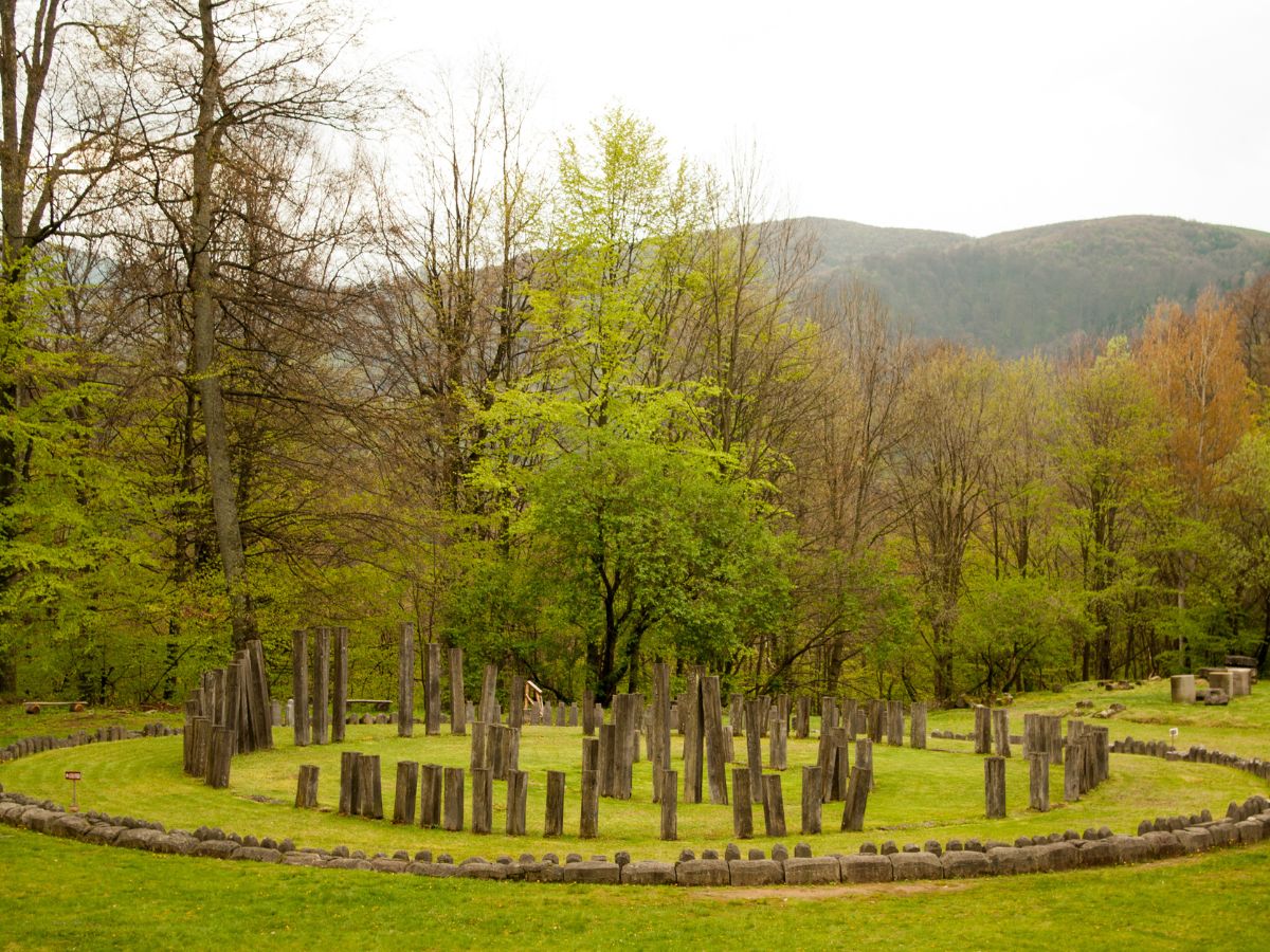 The Romanian Stonehenge at Sarmizegetusa on green fields surrounded by tall trees under bright sky in Transylvania