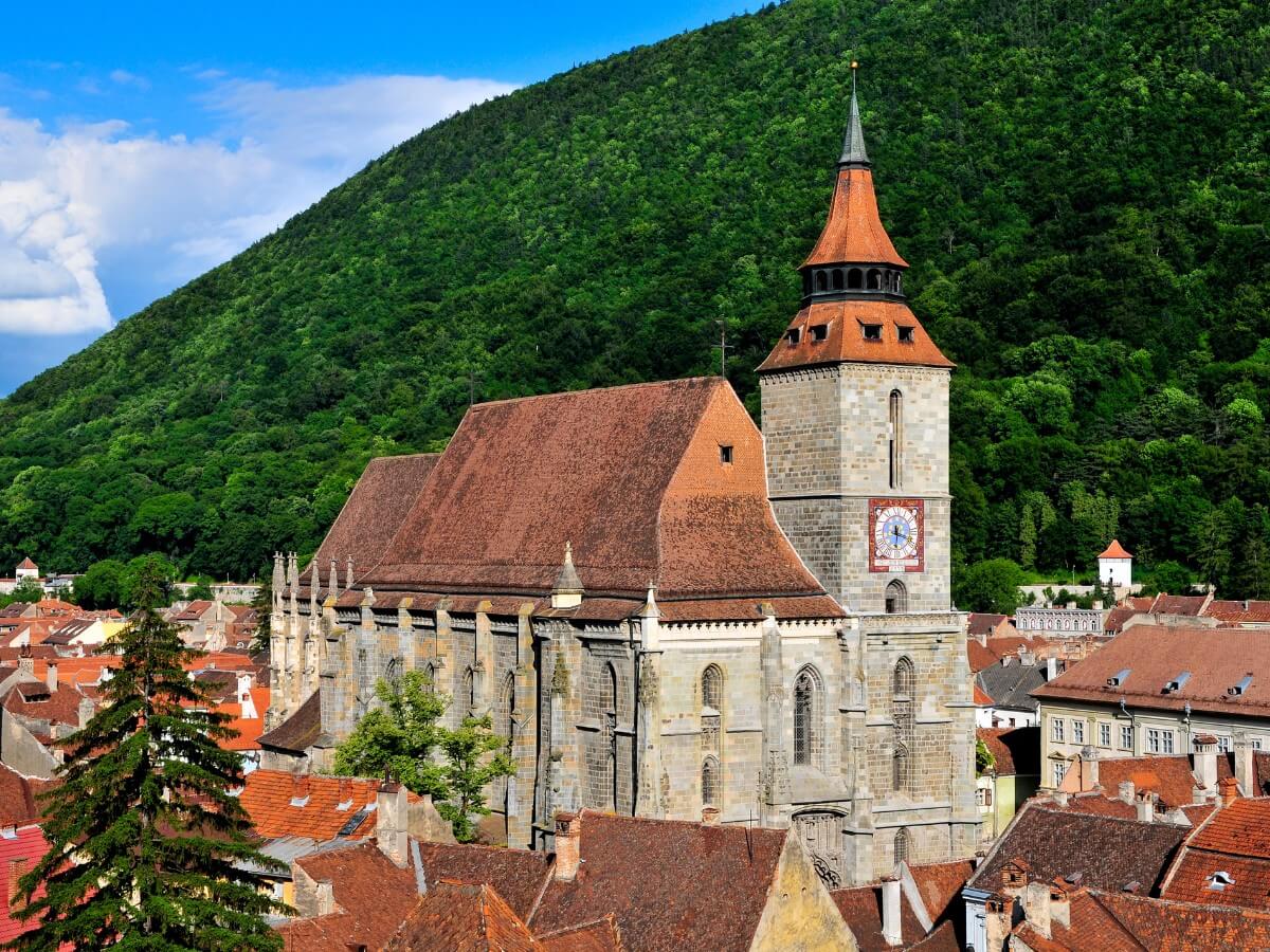 The Biserica Neagră or Black Church in Brasov surrounded by buildings with a backdrop of tree covered mountains in Brasov