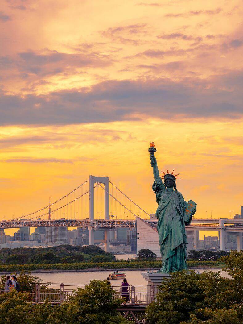 Odaiba at sunset with the statue of liberty and the bridge behind it