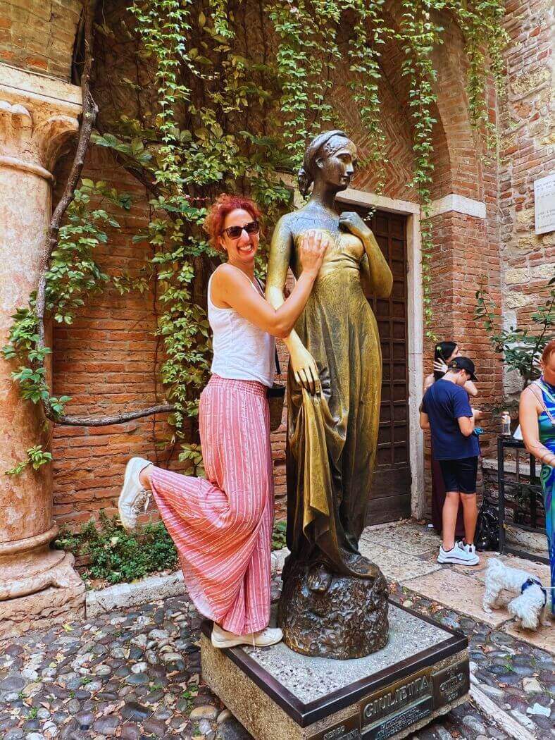 Estatua de Julieta con una mujer sonriendo tocándola.